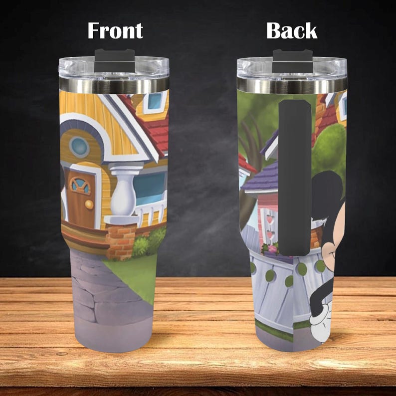 May include: A stainless steel tumbler featuring a colorful cartoon house design on the front and a cartoon character on the back. The tumbler has a clear lid and a black handle. The design includes yellow, red, and blue colors.