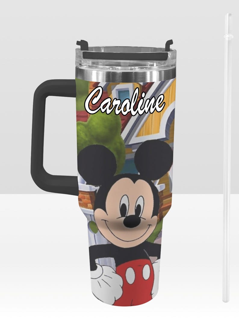 May include: A stainless steel tumbler featuring Mickey Mouse with a black handle and lid. The tumbler has a cartoon background and the name "Caroline" in script. Includes a clear straw.