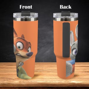 May include: An orange insulated tumbler featuring characters from Zootopia. The front displays Nick Wilde, while the back shows Judy Hopps. The tumbler has a clear lid and a black handle. The design is printed on the tumbler's orange surface.