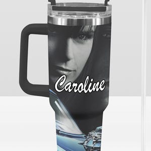 May include: Black and silver insulated tumbler with a black handle and a clear straw. The tumbler features a black and white image of a woman's face with the name "Caroline" in white script. A blue car is at the bottom.