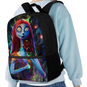 May include: A black backpack featuring a vibrant, colorful graphic print of a blue-skinned character with long red hair holding a single red rose. The backpack has black straps, a zippered main compartment, and a front pocket with a black zipper.