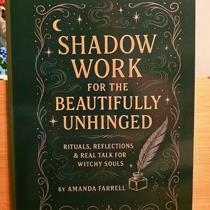 May include: A hardcover book titled "SHADOW WORK for the BEAUTIFULLY UNHINGED" with gold lettering and decorative flourishes on a dark green background. The cover features a quill and inkwell illustration. The book is about rituals, reflections, and real talk for witchy souls.
