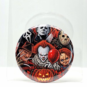 May include: A circular pinback button featuring a colorful graphic illustration of various horror movie characters, including a clown with a red balloon, a masked figure, a hockey mask wearer, and a jack-o'-lantern against a red background.