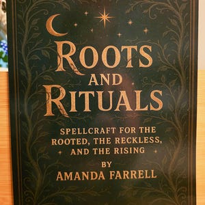 May include: A book titled "Roots and Rituals" with a dark green cover and gold lettering. The cover features a crescent moon, stars, and decorative vines. The author's name, Amanda Farrell, is also displayed.