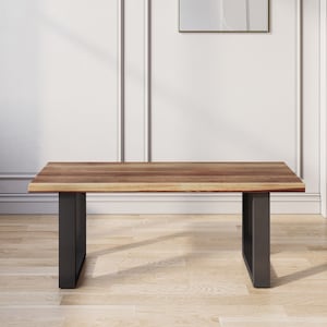 May include: A wooden coffee table with a natural wood finish and black metal legs. The table is sitting on a wooden floor.