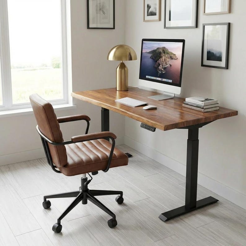 May include: A modern home office setup featuring a brown wooden desk with a black adjustable base, a brown leather office chair, and a gold-colored desk lamp. A computer monitor, keyboard, and mouse sit on the desk. The chair has a black frame and rolling wheels.