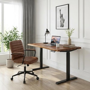 May include: A home office setup featuring a brown wooden desk with black legs, a brown leather office chair, and a laptop. A black framed picture of the Statue of Liberty hangs on the white wall. A black desk lamp and a potted plant are also visible.