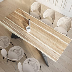 May include: A long, wooden dining table with a natural wood grain pattern and a black metal base. Six beige chairs with a unique fan-shaped back design surround the table.