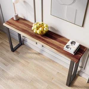 May include: A long, narrow wooden console table with a live edge top and black metal legs. The table is decorated with a bowl of yellow lemons and a stack of books.