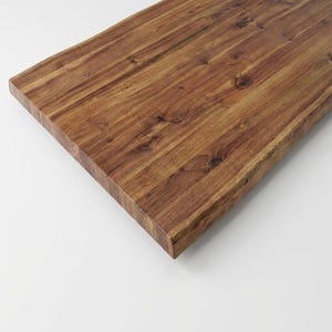 May include: A rectangular wooden tabletop with a rich, warm brown color. The wood grain is prominently displayed, with visible knots and variations in tone. The edge of the table is squared off, and the surface appears smooth and finished.