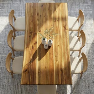 May include: Overhead view of a rectangular wooden dining table with eight cream-colored upholstered chairs. The table is adorned with three small white vases holding greenery, set on a light gray rug.