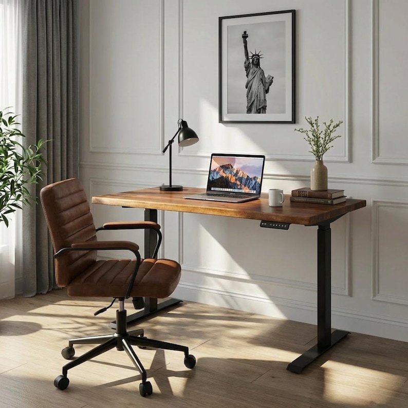 May include: A home office setup featuring a brown wooden desk with black legs, a brown leather office chair, and a laptop. A black and white framed picture of the Statue of Liberty hangs on the wall. A black desk lamp and a vase with greenery are on the desk.