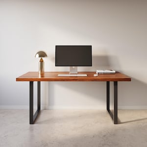 May include: A wooden desk with black metal legs. A computer monitor, keyboard, and lamp are on the desk. A book titled "The Modern" is on the desk.