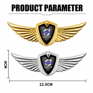 Puede incluir: Dos emblemas de coche Volvo con un escudo central y alas que se extienden a cada lado. Un emblema es de tono dorado y el otro de tono plateado. Ambos muestran el logotipo y el texto de Volvo. Las dimensiones son de 4 cm por 12,5 cm.