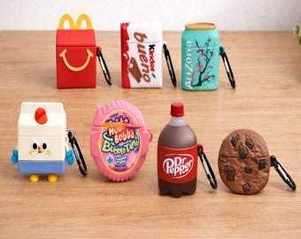 May include: A selection of brightly coloured AirPod cases, each designed to look like a different food or drink. The cases include a red McDonald's Happy Meal, a Kinder Bueno bar, an Arizona iced tea can, a milk carton, Hubba Bubba bubble tape, a Dr. Pepper bottle, and a chocolate chip cookie.