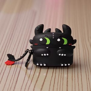 Puede incluir: Funda protectora negra para auriculares inalámbricos, con forma de dragón de dibujos animados. La funda tiene ojos verdes, detalles blancos y una cola roja y negra. Se adjunta un pequeño anillo de metal.