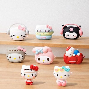 May include: A selection of brightly coloured AirPod cases featuring cartoon characters. Designs include a white Hello Kitty case with headphones, a stacked pastel case with the word "Cute", and a black case with a skull and headphones. Other cases feature various characters.
