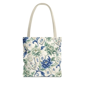 May include: Tote bag with a cream-colored handle and a floral pattern. The pattern features blue and green peonies, leaves, and Mahjong tiles with Chinese characters. The bag is white with a cream-colored handle.