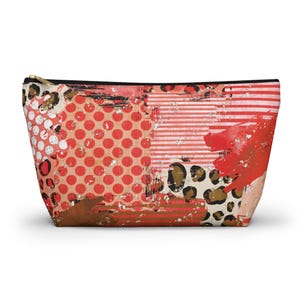 Op de afbeelding: Een rechthoekige make-uptas met een zwarte ritssluiting. De tas heeft een collage-ontwerp met rode stippen, strepen en luipaardprints. Het kleurenpalet omvat rood, bruin en beige.