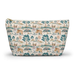 May include: A beige zippered pouch with a repeating pattern of corgi dogs in a landscape with trees and flowers. The corgis have brown and white fur and wear pink bow ties. The background includes teal and brown trees, and pink flowers.