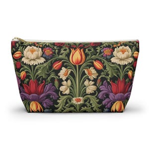 May include: A black zippered pouch with a floral pattern. The pattern features red, yellow, orange, white, and purple flowers on a dark green background.