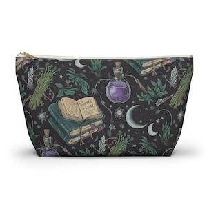 Puede incluir: Una bolsa con cremallera negra y verde con un patrón repetido de libros, frascos de pociones, hierbas y lunas crecientes. El texto "Spell Book" es visible en uno de los libros.