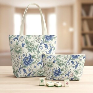May include: A tote bag and a matching zippered pouch feature a floral pattern with blue and green peonies and Mahjong tiles on a cream background. The tote bag has cream-colored handles. Four Mahjong tiles are in front.