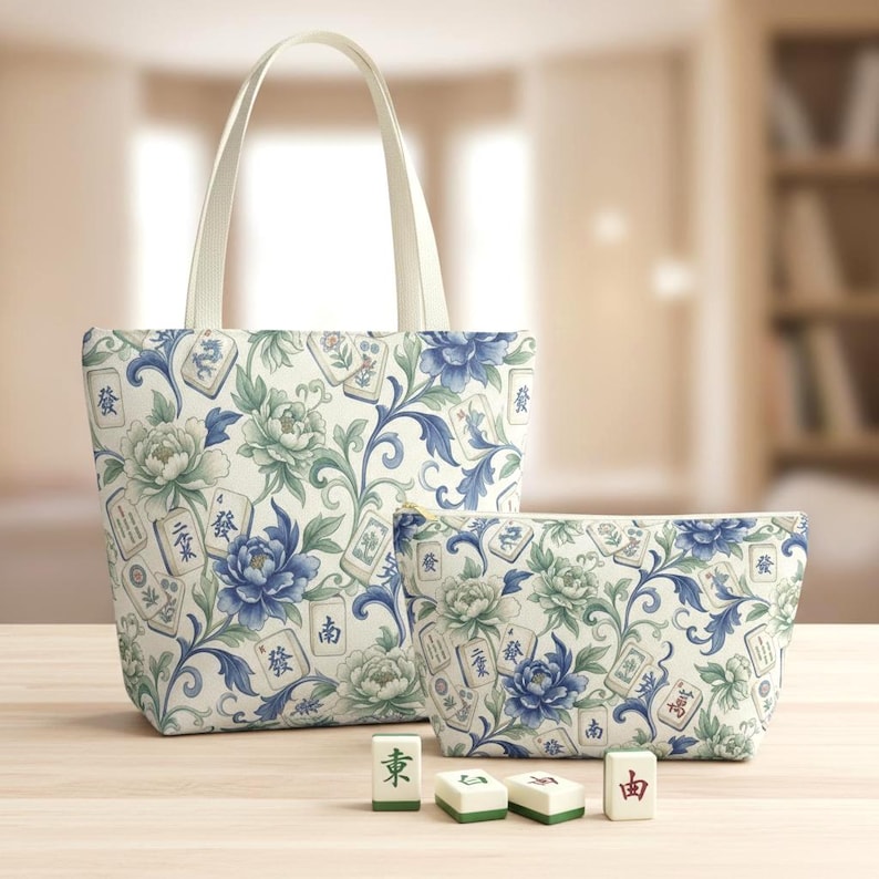 May include: A tote bag and a matching zippered pouch feature a floral pattern with blue and green peonies and Mahjong tiles on a cream background. The tote bag has cream-colored handles. Four Mahjong tiles are in front.