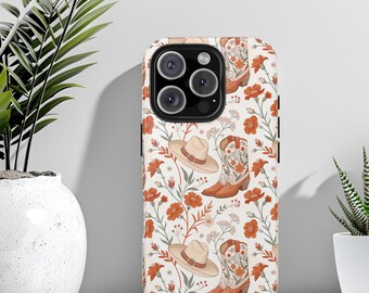 May include: A white iPhone case with a floral pattern featuring cowboy boots and hats. The boots and hats are brown and white with floral details. The background is white with orange flowers.