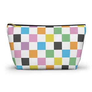 May include: A colorful zippered pouch with a checkerboard pattern. The pattern features squares of white, black, pink, orange, yellow, green, blue, and purple. The zipper is gold-colored.