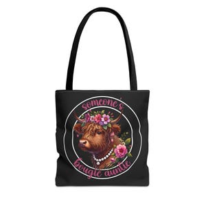 Può includere: Borsa tote nera con un cerchio bianco e testo rosa che dice "someone's bougie auntie". All'interno del cerchio c'è una mucca Highland marrone e bianca con una corona di fiori rosa e una collana di perle.