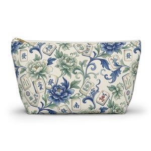 Pode incluir: Bolsa com zíper creme com um padrão floral e de peças de Mahjong em tons de azul e verde. O design inclui peónias e volutas. A bolsa tem um zíper dourado.