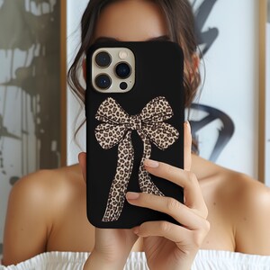 May include: A black phone case with a leopard print bow design. The case has a camera lens cutout and a black background.
