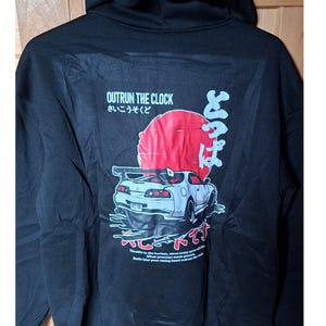 Könnte beinhalten: Schwarzer Hoodie mit einer Grafik eines weißen Sportwagens, einer roten Sonne und japanischem Text. Der Text "Outrun the Clock" befindet sich über der Grafik. Zusätzlicher Text unten lautet "Throttle to the horizon..."
