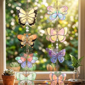 May include: A collection of colorful stained glass butterfly suncatchers hanging in front of a window. Each butterfly features a unique design with various colors, including yellow, orange, pink, purple, and blue. They are suspended by chains with crystal accents.