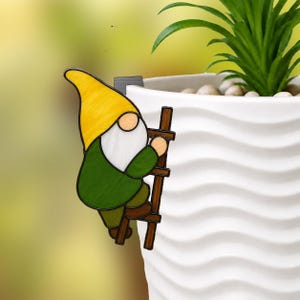 May include: A colorful gnome climbing a wooden ladder, designed to hang on the edge of a white planter. The gnome has a yellow hat, white beard, green jacket, and brown pants. The ladder is brown.