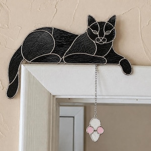Peut inclure: Une figurine de chat en vitrail noir conçue pour être posée sur un coin, avec des segments de verre noir texturé reliés par des lignes de soudure en métal argenté. Une petite souris en vitrail blanc et rose pend au chat par une chaîne.
