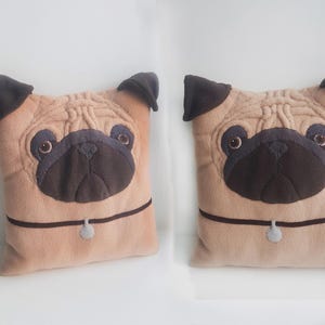 Puede incluir: Dos cojines de peluche con dise&ntilde;o de pug. Los cojines son de color beige con orejas, hocicos y ojos de color marr&oacute;n oscuro. Cada coj&iacute;n tiene un collar marr&oacute;n oscuro con un peque&ntilde;o dije gris. Los cojines son cuadrados y tienen un aspecto suave y texturizado.