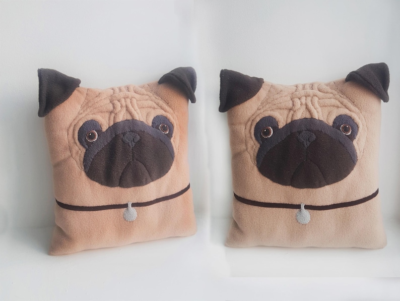 Puede incluir: Dos cojines de peluche con dise&ntilde;o de pug. Los cojines son de color beige con orejas, hocicos y ojos de color marr&oacute;n oscuro. Cada coj&iacute;n tiene un collar marr&oacute;n oscuro con un peque&ntilde;o dije gris. Los cojines son cuadrados y tienen un aspecto suave y texturizado.