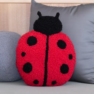 May include: A red and black ladybug-shaped decorative pillow. The pillow has a textured, plush surface with black spots and a black head. The ladybug pillow is a whimsical accent for a child's room or a nature-themed space.