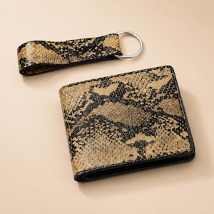 May include: A bi-fold wallet and a keychain, both with a snakeskin pattern in tan, brown, and black. The wallet is rectangular with a black border. The keychain has a silver ring.