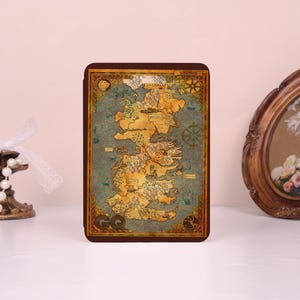 May include: A rectangular e-reader cover featuring a detailed fantasy map of Westeros. The map displays landmasses in shades of tan and brown against a blue ocean background, with compass roses, small ship illustrations, and the text Westeros.