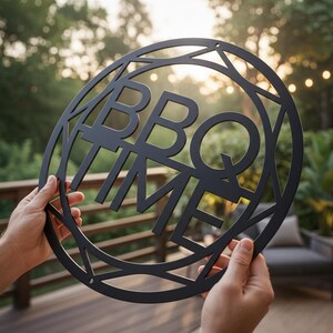Könnte beinhalten: Ein kreisförmiges schwarzes Metallschild mit dem ausgeschnittenen Text BBQ TIME in fetten Großbuchstaben. Das Design umfasst einen geometrischen Rahmen mit winkligen Linien, die die Buchstaben mit dem äußeren Rand verbinden.