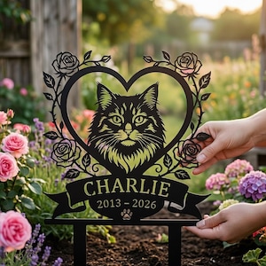 Könnte beinhalten: Schwarzer Metall-Gartenstecker mit einer Katzensilhouette in einem herzförmigen Rahmen, verziert mit Rosen. Der Name "Charlie" und die Daten 2013-2026 sind auf einem Banner unter dem Katzenbild mit einem Pfotenabdruck-Symbol abgebildet.