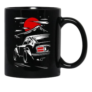 May include: Black ceramic mug featuring a white illustration of a classic sports car with a red sun and mountain range in the background. The car is depicted from the rear, with details like taillights and exhaust pipes visible.