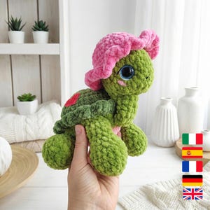 May include: A handmade green crochet turtle with a pink flower hat and blue eyes. The turtle has a heart-shaped patch on its back. The plush toy is soft and cuddly, perfect for a child's room or as a unique gift.