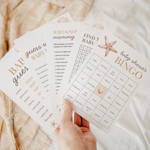 May include: A collection of baby shower games printed on white cardstock. The games include "Baby Bingo", "Who Knows Mommy", and "Baby Guess". The designs feature seashell and starfish illustrations in a neutral color palette.