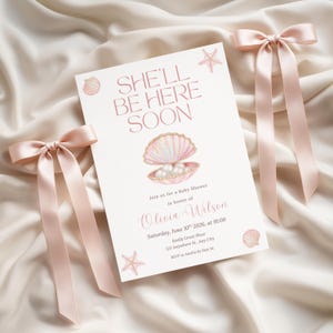 May include: A baby shower invitation with the text "SHE'LL BE HERE SOON" in pink script. The invitation features a seashell illustration with pearls and is adorned with pink starfish and seashell graphics. Two pink satin bows are placed on either side.