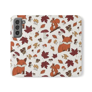 Op de afbeelding: Een witte telefoonhoes met een herhalend patroon van oranje vossen, eekhoorns, paddenstoelen en herfstbladeren in tinten rood, bruin en geel. De hoes heeft een camera-uitsparing aan de linkerkant.