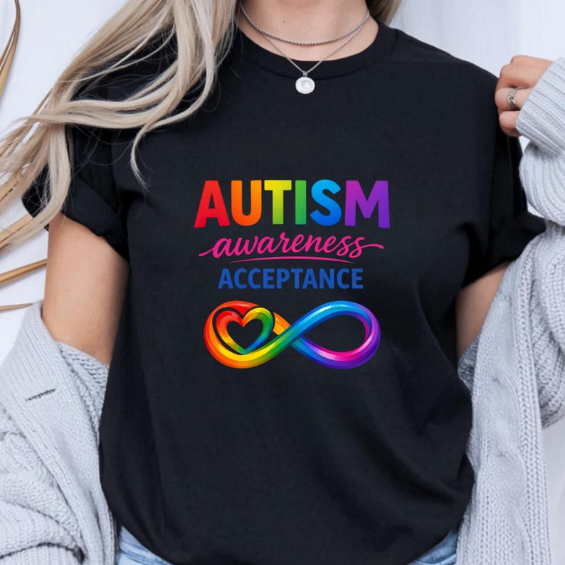 May include: Black t-shirt with the words "AUTISM awareness ACCEPTANCE" in rainbow colors. The design includes a rainbow heart intertwined with an infinity symbol. The shirt is a crew neck.